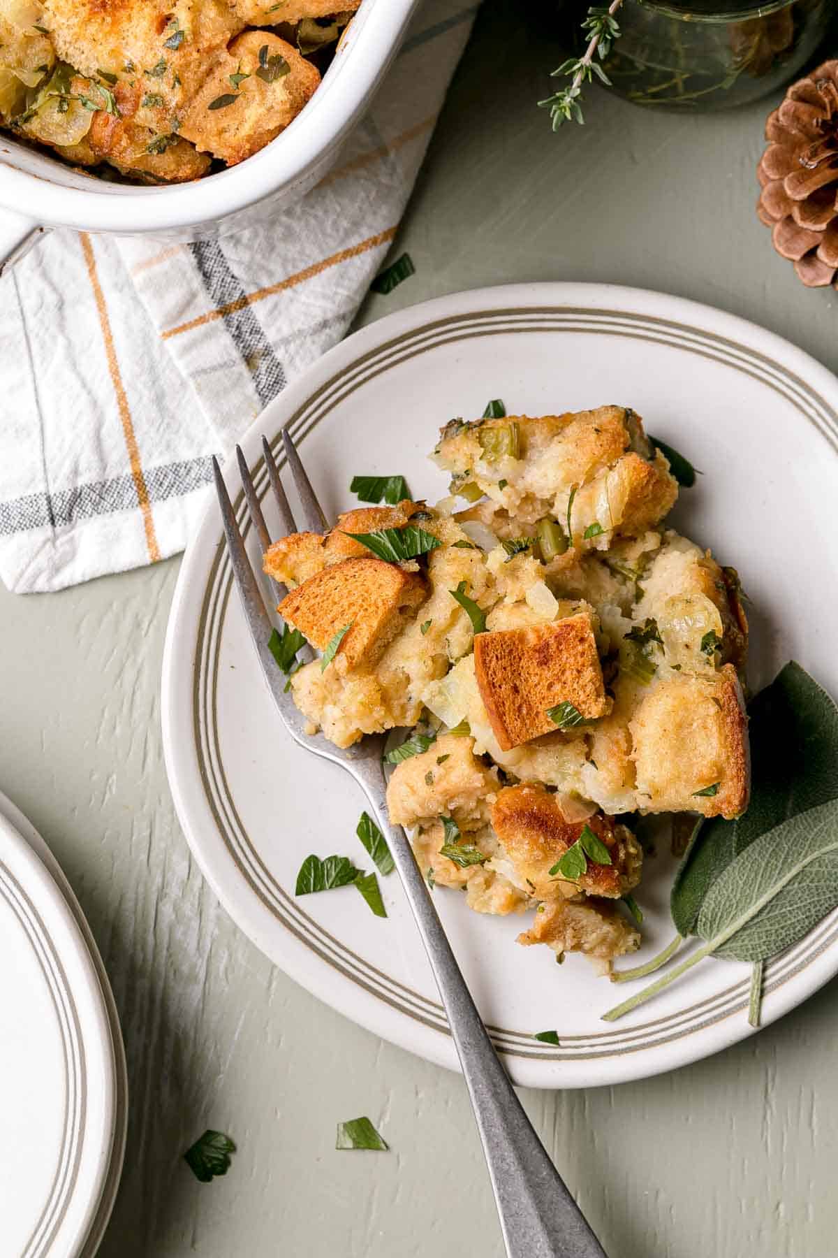 A serving of gluten-free stuffing on a small plate with a fork and sage leaves.