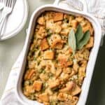 White Staub casserole dish with baked gluten free stuffing and sage leaves on top.