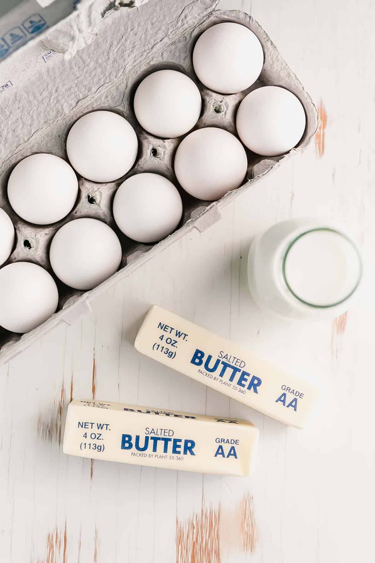 Milk, eggs, and butter on white wooden surface.