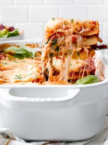 A slice of gluten-free lasagna lifted from a pan with cheese pull.