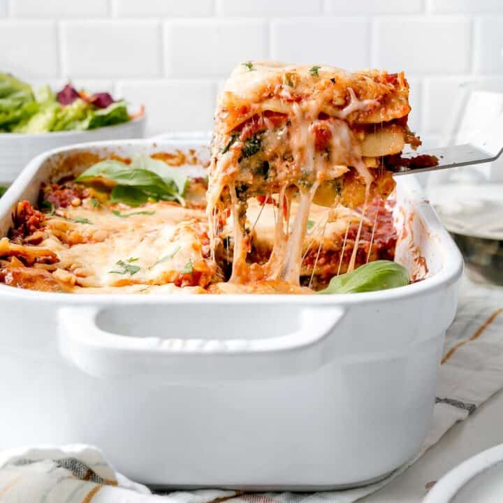 A slice of gluten-free lasagna lifted from a pan with cheese pull.