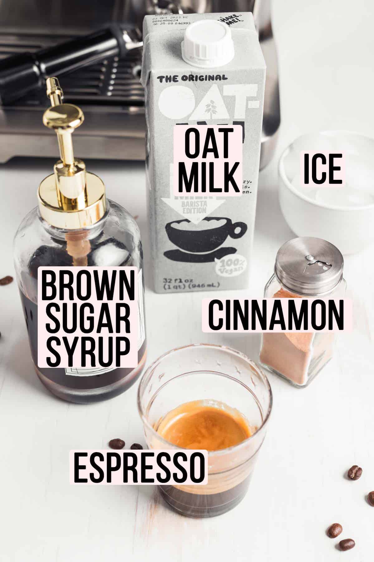 Espresso in a glass, jar of cinnamon, box of oat milk, brown sugar syrup in a jar, and ice in a bowl in front of an espresso machine.