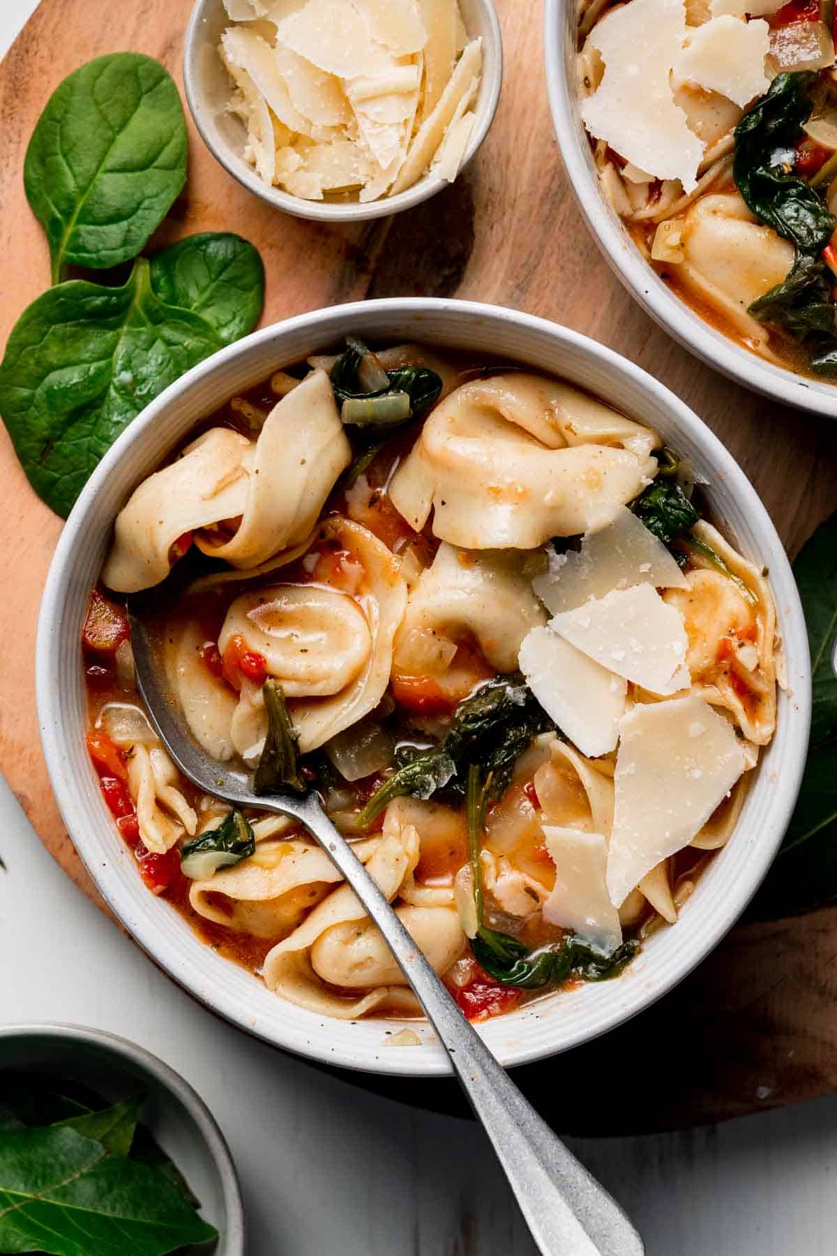 A bowl with tortellini and wilted spinach in a tomato broth garnished with parmesan cheese.