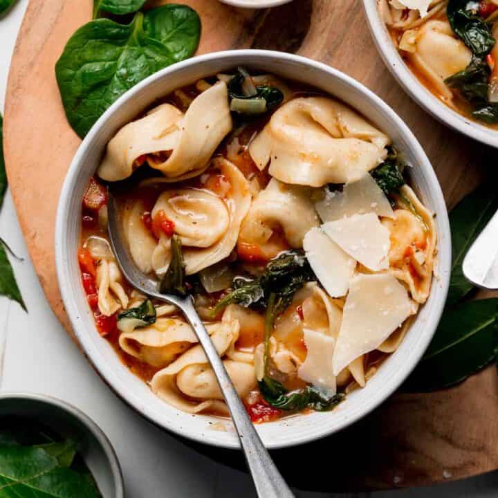 A bowl with tortellini and wilted spinach in a tomato broth garnished with parmesan cheese.
