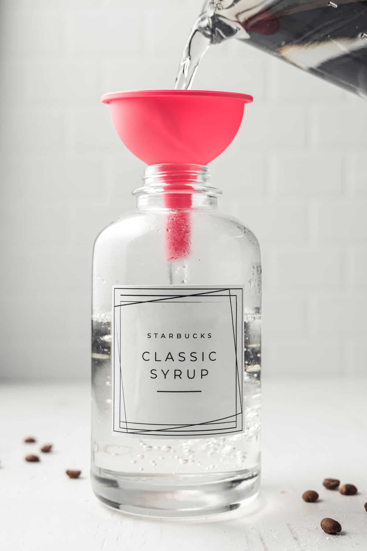 Pouring classic syrup into glass jar using pink funnel.