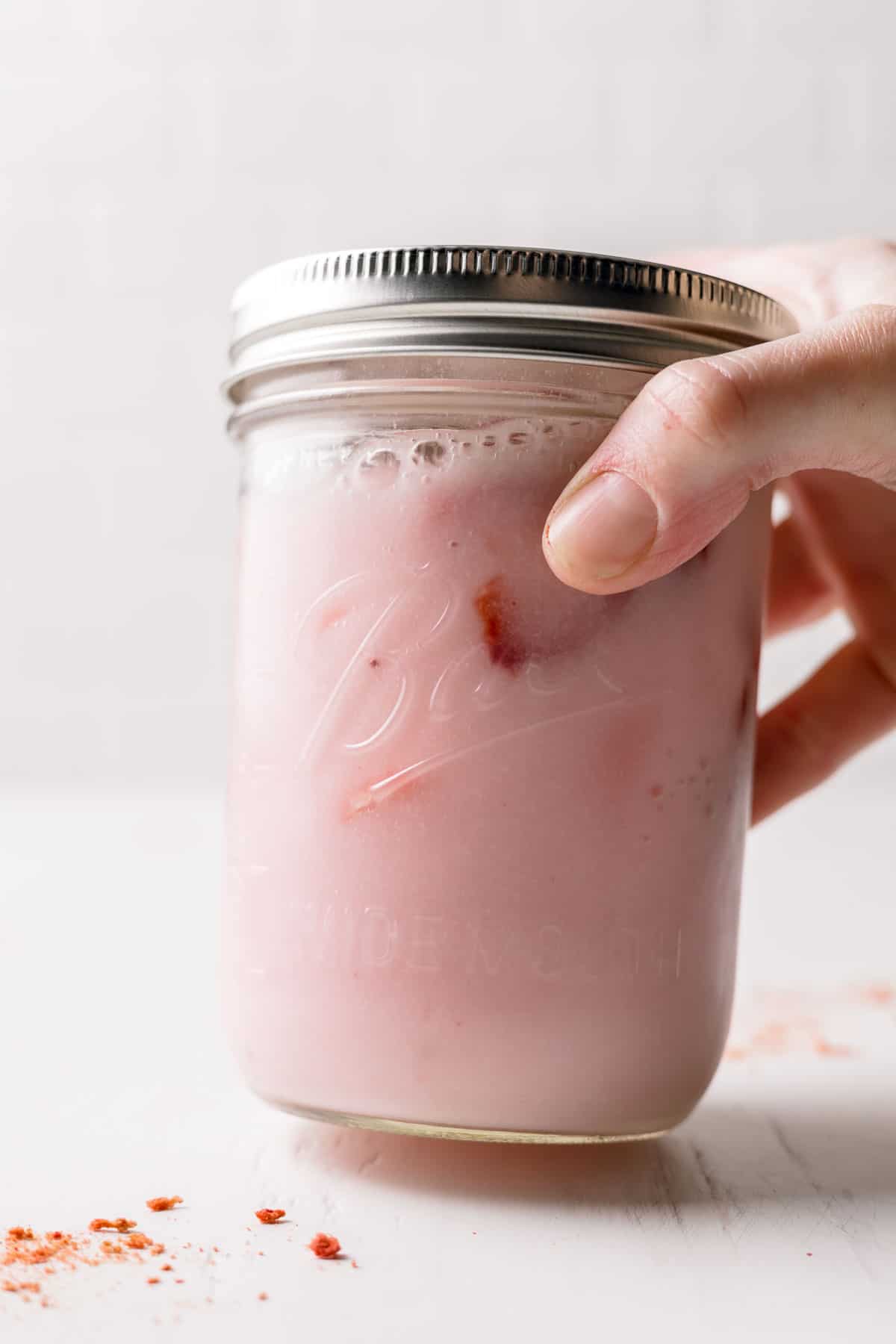 Pink drink in a mason jar with lid, foamy from being shaken.