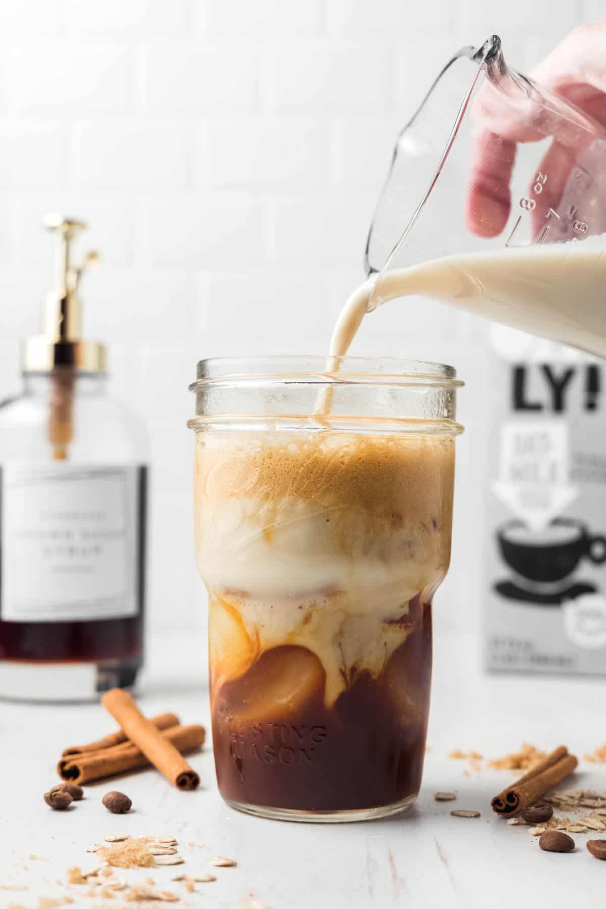 Mason jar with the espresso and ice, pouring oat milk on top.