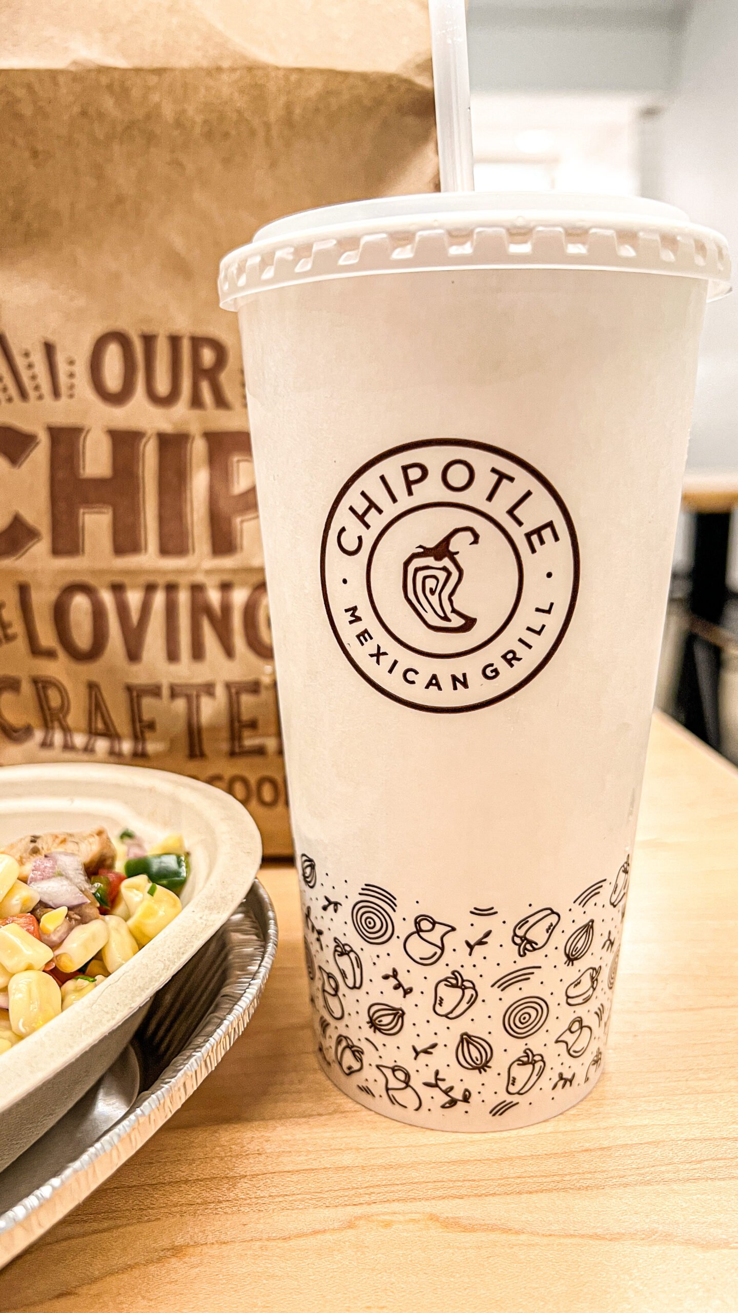 Chipotle fountain drink cup next to a bag of chips and burrito bowl.