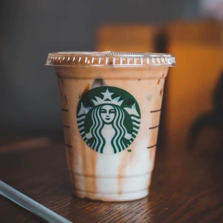 Iced Starbucks drink on wooden table, coffee and milk swirling in cup.
