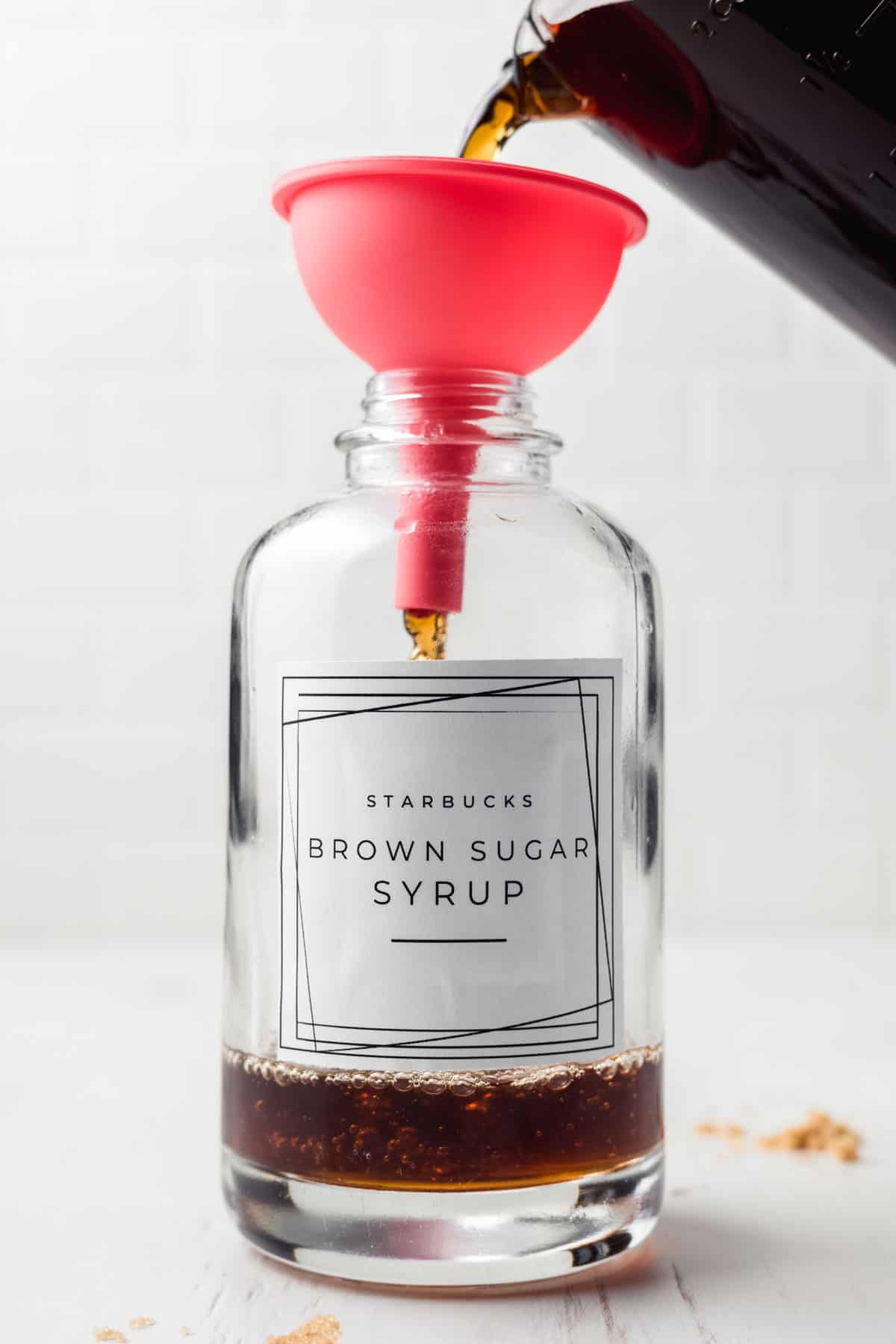 Funnel in glass jar, pouring brown sugar syrup in jar.