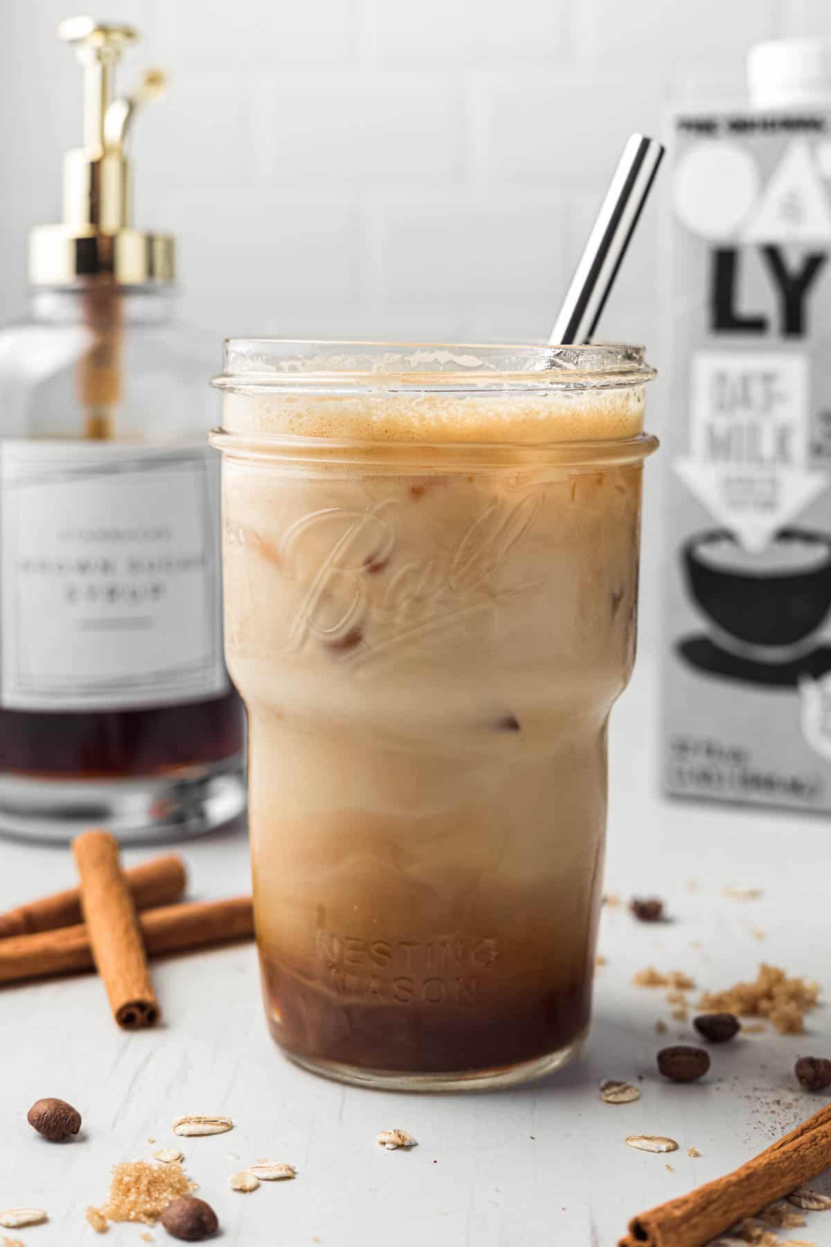 Tall mason jar with dark espresso on the bottom, oat milk on top, and metal straw.