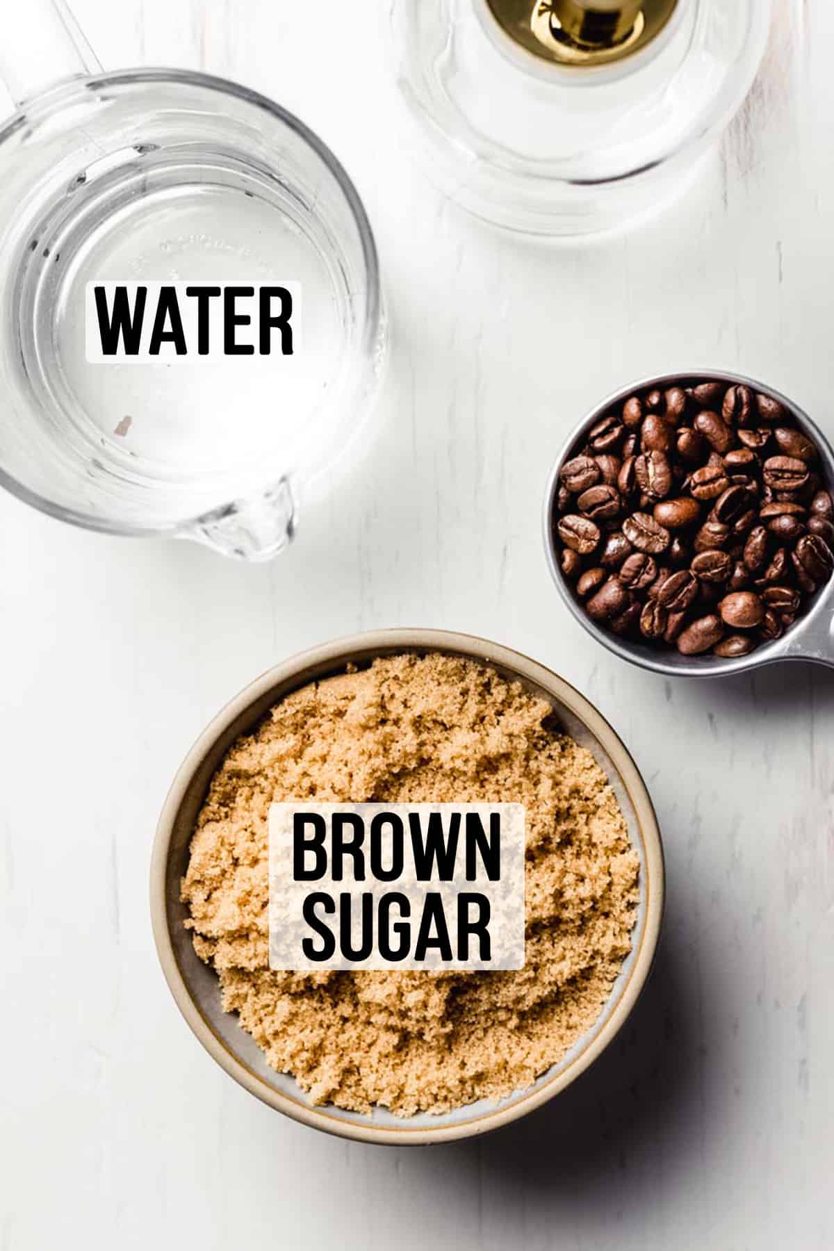 Brown sugar in a bowl next to water in a measuring cup, coffee beans, and a glass jar with pump.