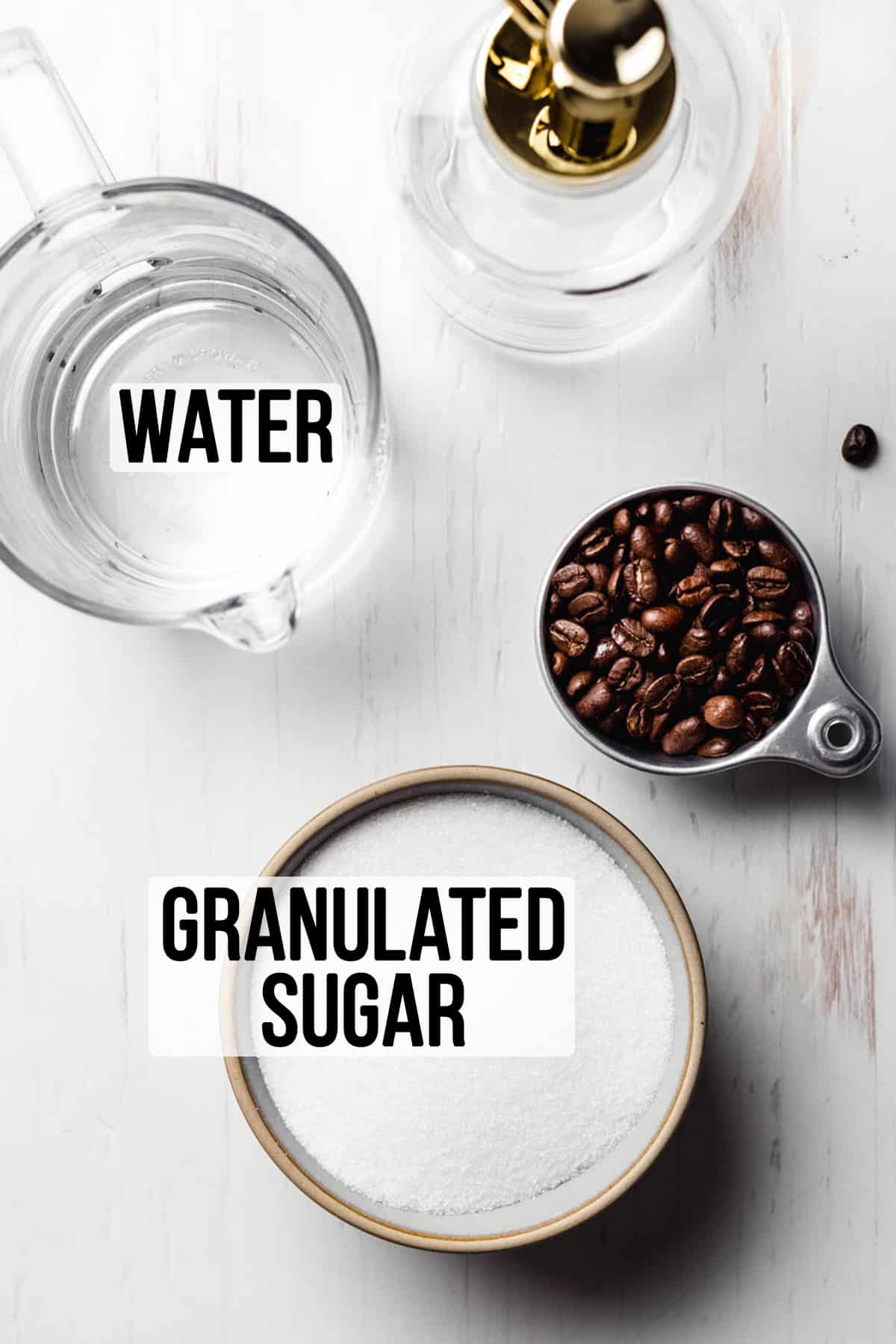 Granulated sugar in a bowl next to a measuring cup with water, coffee beans, and a glass pump jar.