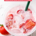 Overhead view of pink drink in reusable Starbucks cup with frothy bubbles and strawberries on top.