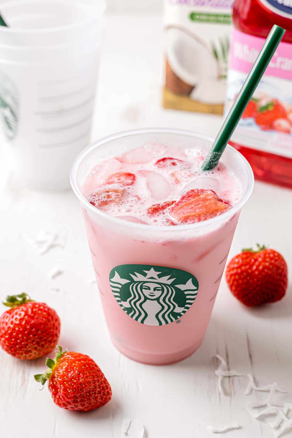 Starbucks copycat pink drink in a Starbucks cup with a green straw next to fresh strawberries.