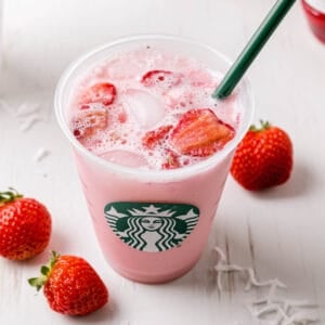 Starbucks copycat pink drink in a Starbucks cup with a green straw next to fresh strawberries.