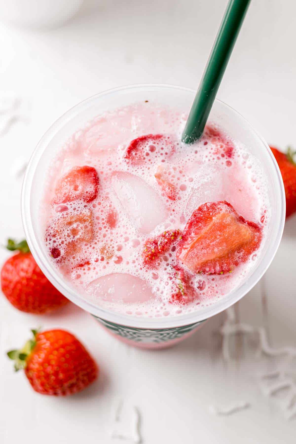 Overhead view of pink drink in reusable Starbucks cup with frothy bubbles and strawberries on top.