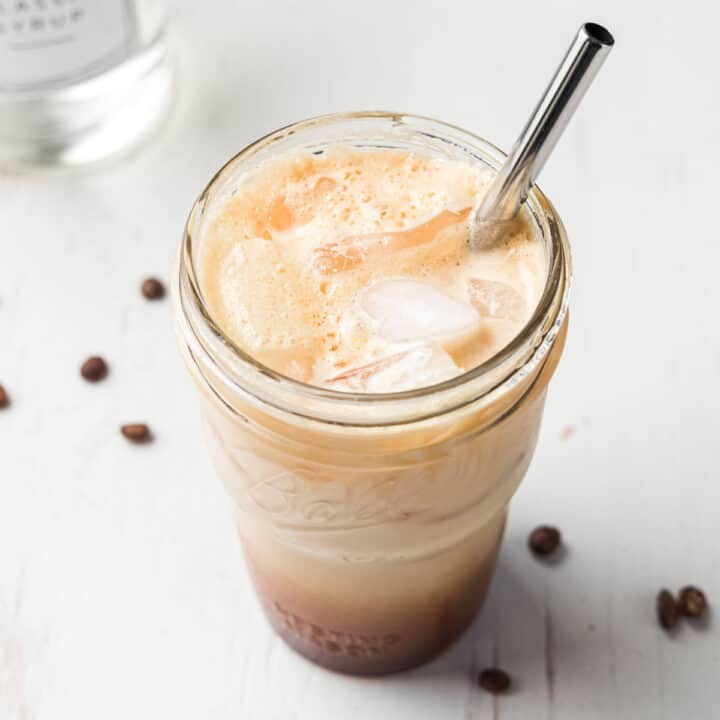 Frothy iced shaken espresso in a mason jar with ice and a stainless steel straw.