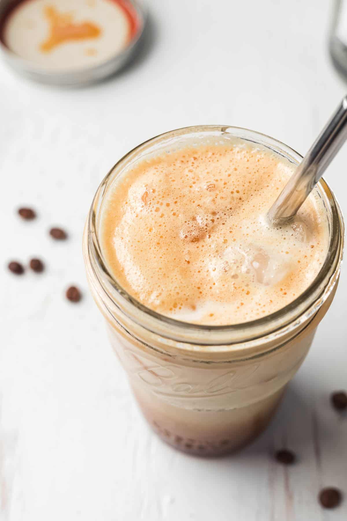 Arial view of mason jar with foam and ice on top of espresso drink, metal straw.