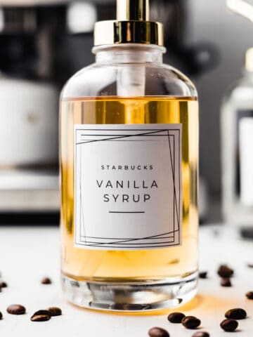 Starbucks vanilla syrup in a glass pump jar surrounded by coffee beans.