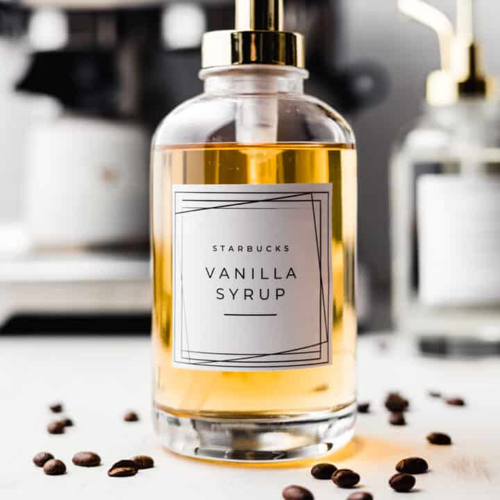 Starbucks vanilla syrup in a glass pump jar surrounded by coffee beans.
