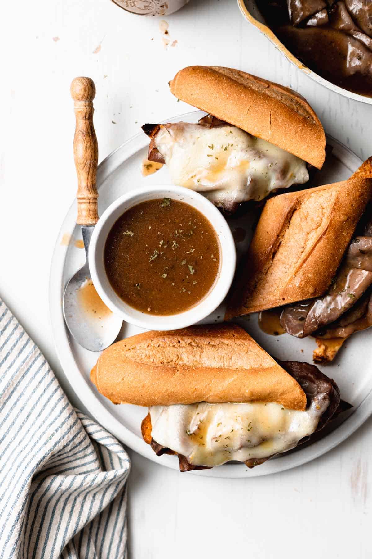 Gluten free au jus in a white ramekin next to French dip sandwiches.