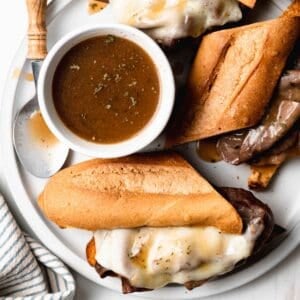 Gluten free au jus in a white ramekin next to French dip sandwiches.