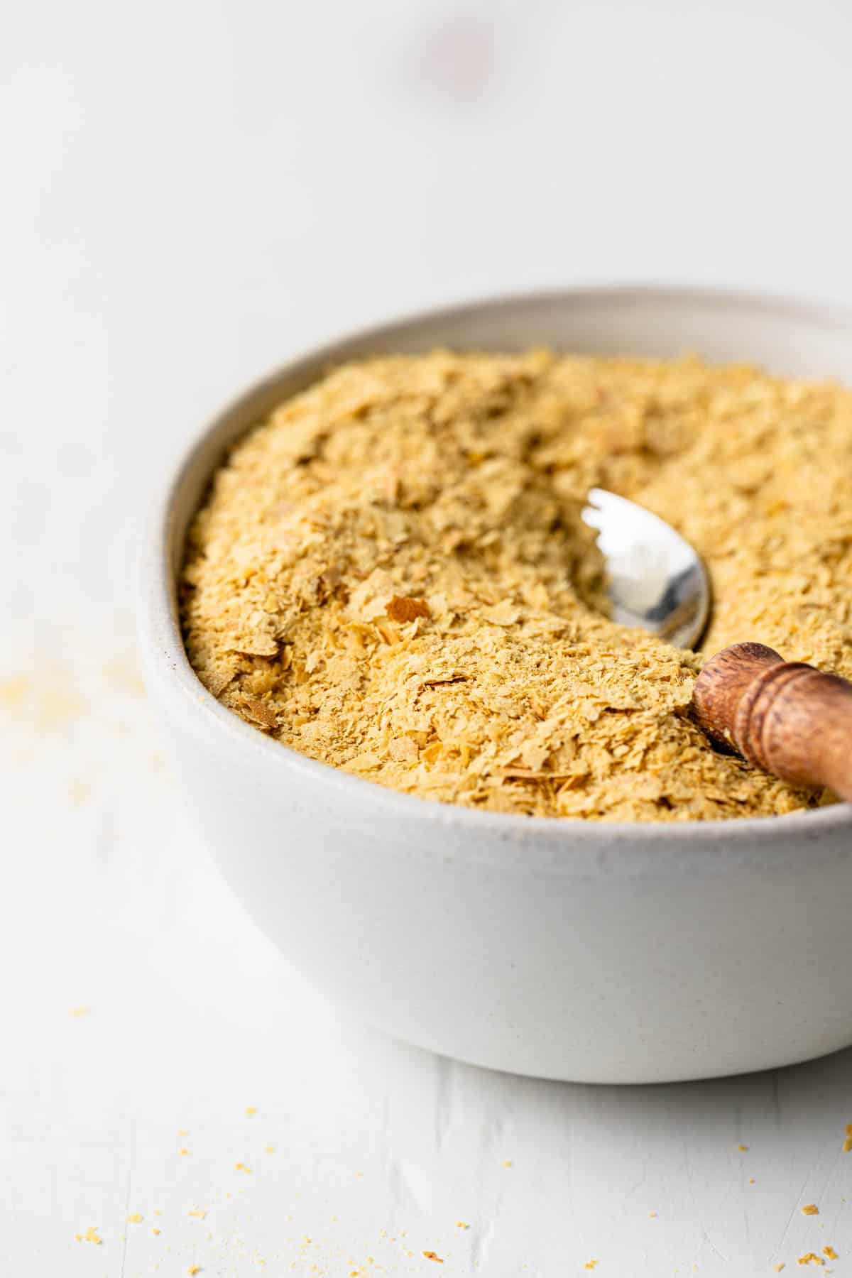 Nutritional yeast flakes in a small bowl with a spoon that has a wooden handle.