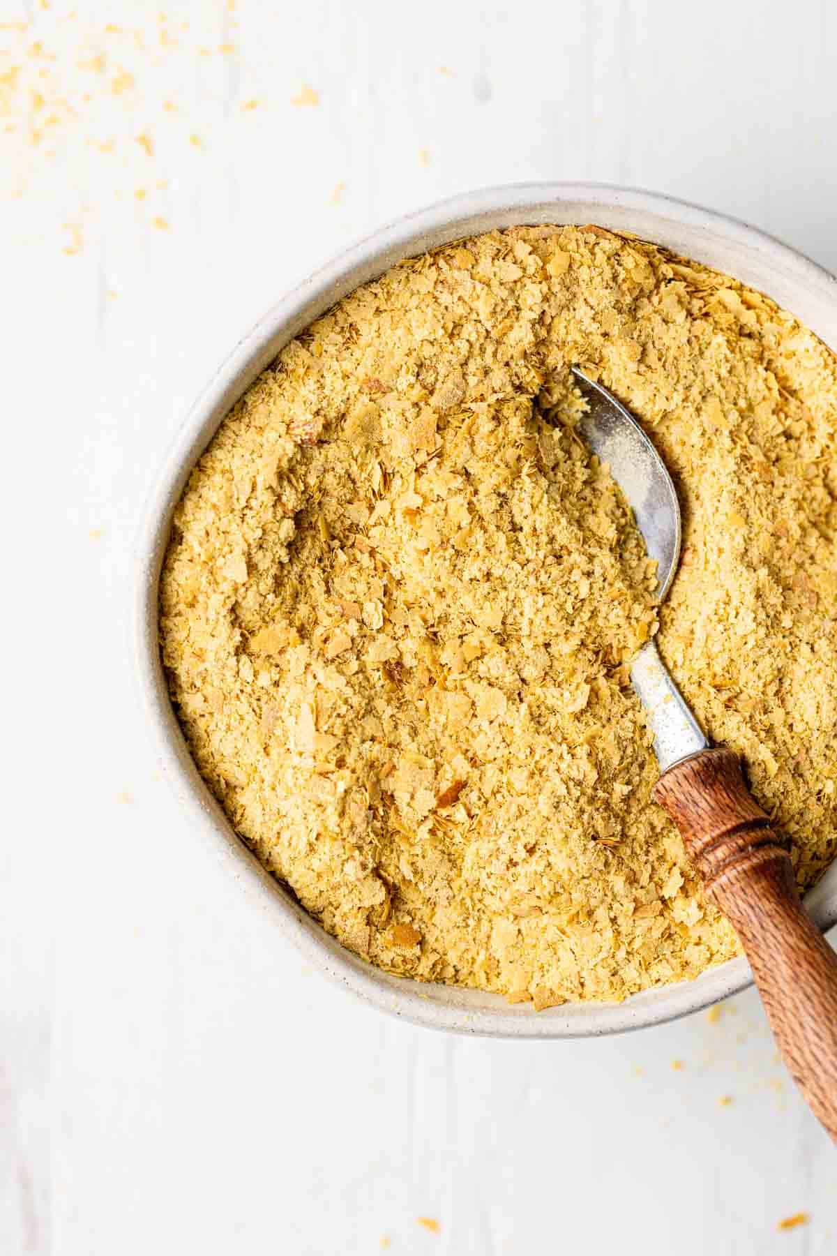 Nutritional yeast flakes in a small bowl with a spoon that has a wooden handle.