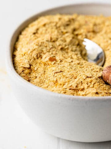 Nutritional yeast flakes in a small bowl with a spoon that has a wooden handle.
