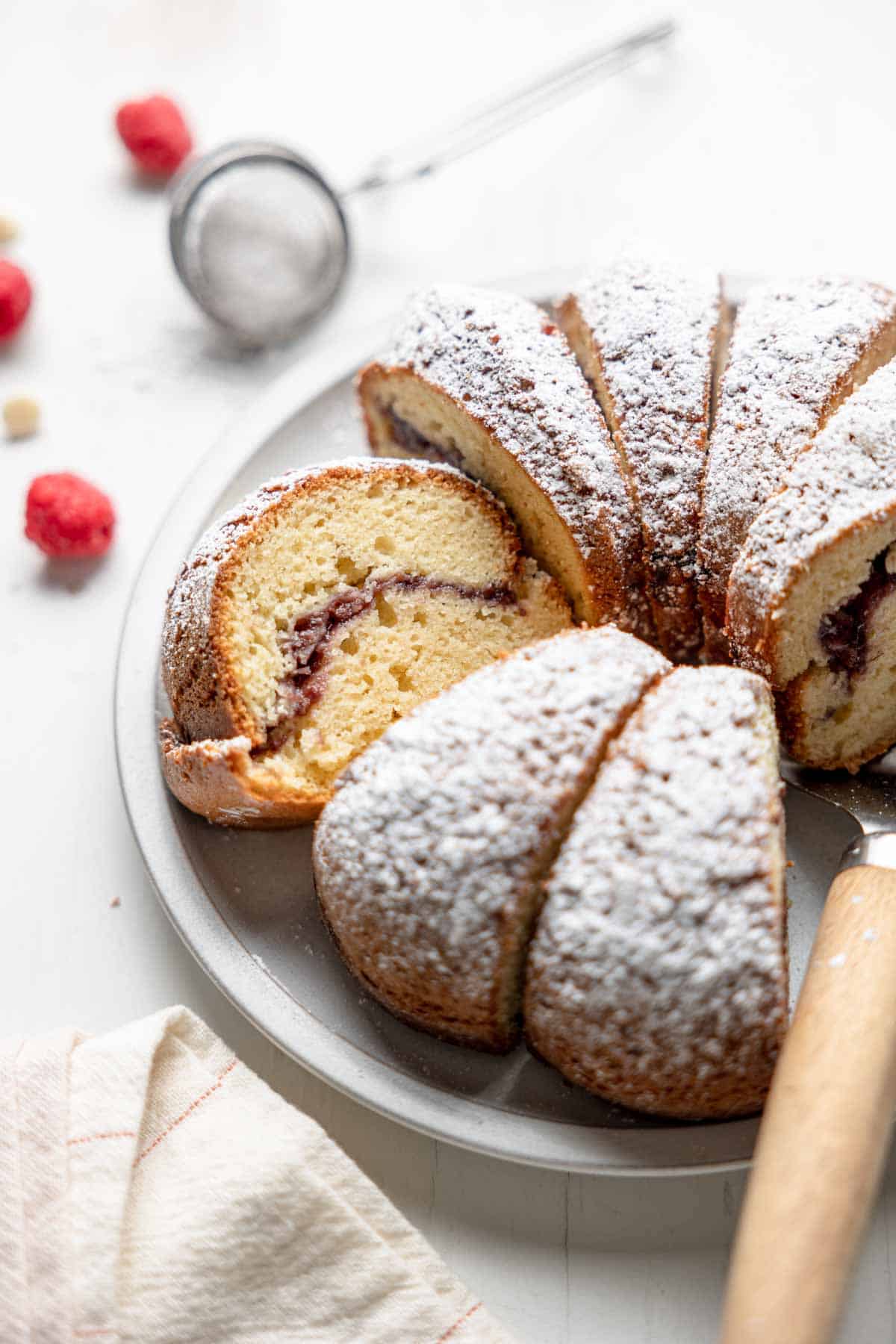 White chocolate raspberry bundt cake dusted with powdered sugar, sliced on a serving plate.