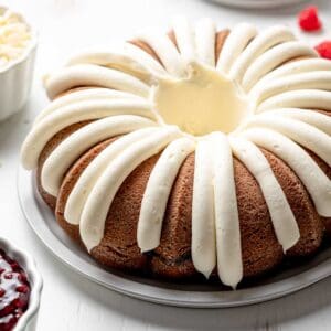 Bundt cake with cream cheese icing piped around the cake next to raspberries and white chocolate chips.