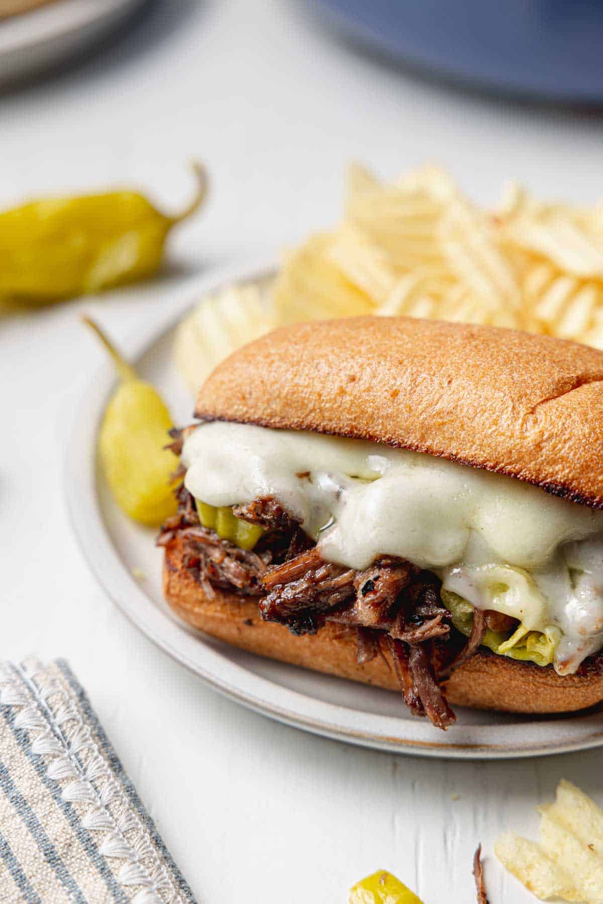 Italian beef sandwich with melted provolone cheese on small plate next to peperoncini peppers.