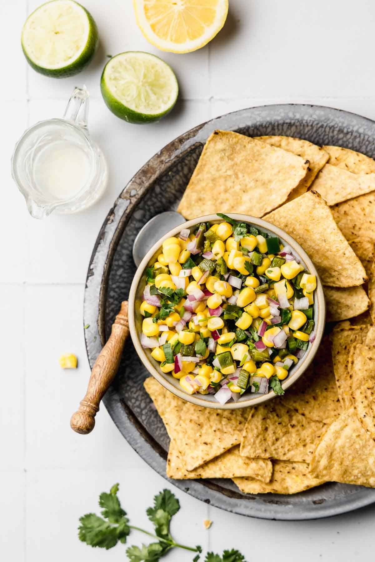 Roasted chili corn salsa in small bowl next to tortilla chips and cilantro.