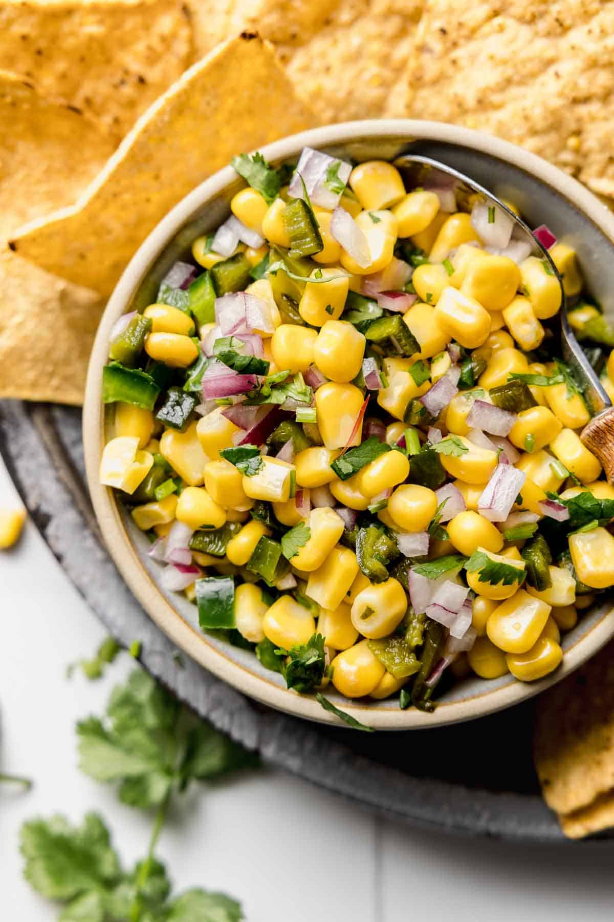 Chipotle roasted chili corn salsa in small bowl next to tortilla chips and cilantro.