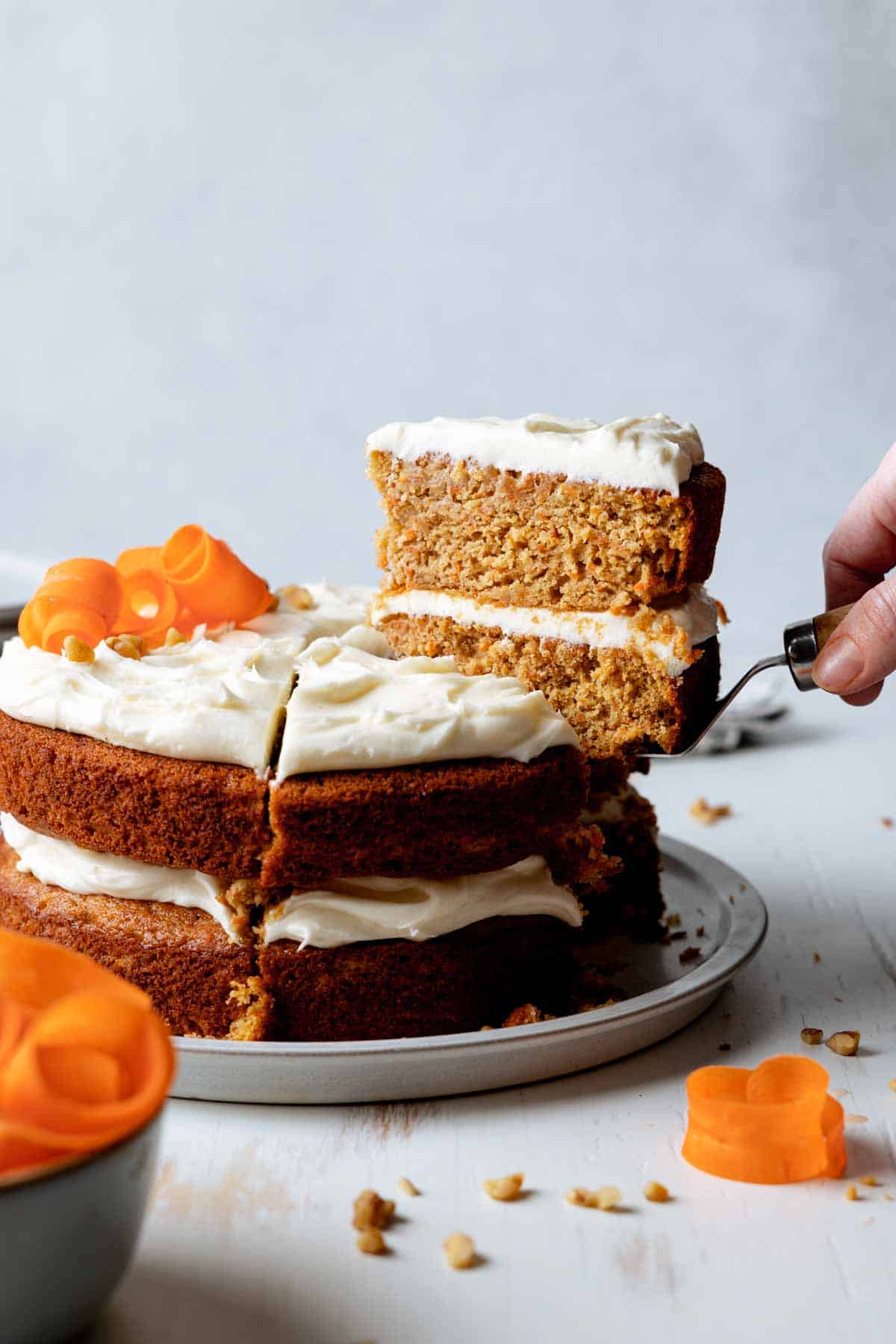 Slice of carrot cake is lifted from the rest of the cake on a spatula. 