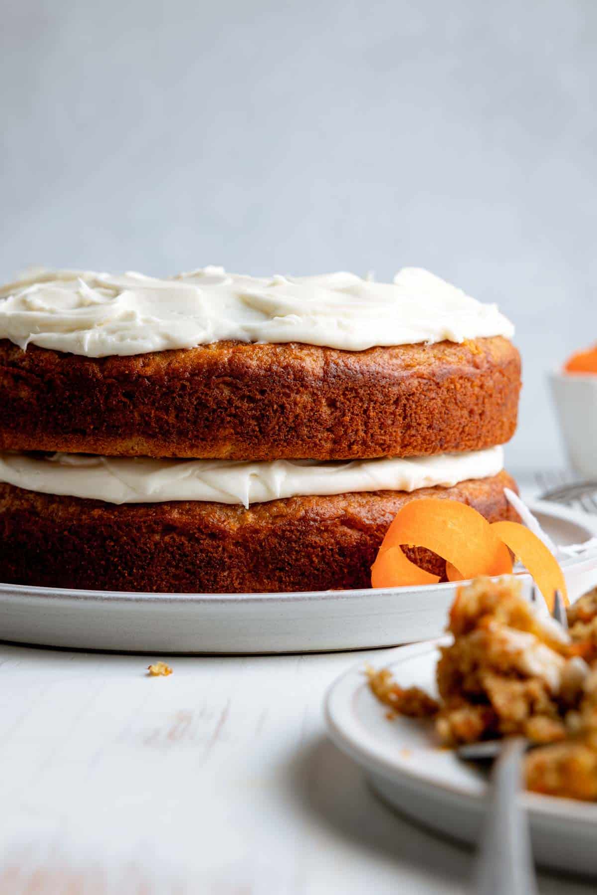 Two layer carrot cake with cream cheese icing on top of each layer but sides are exposed.