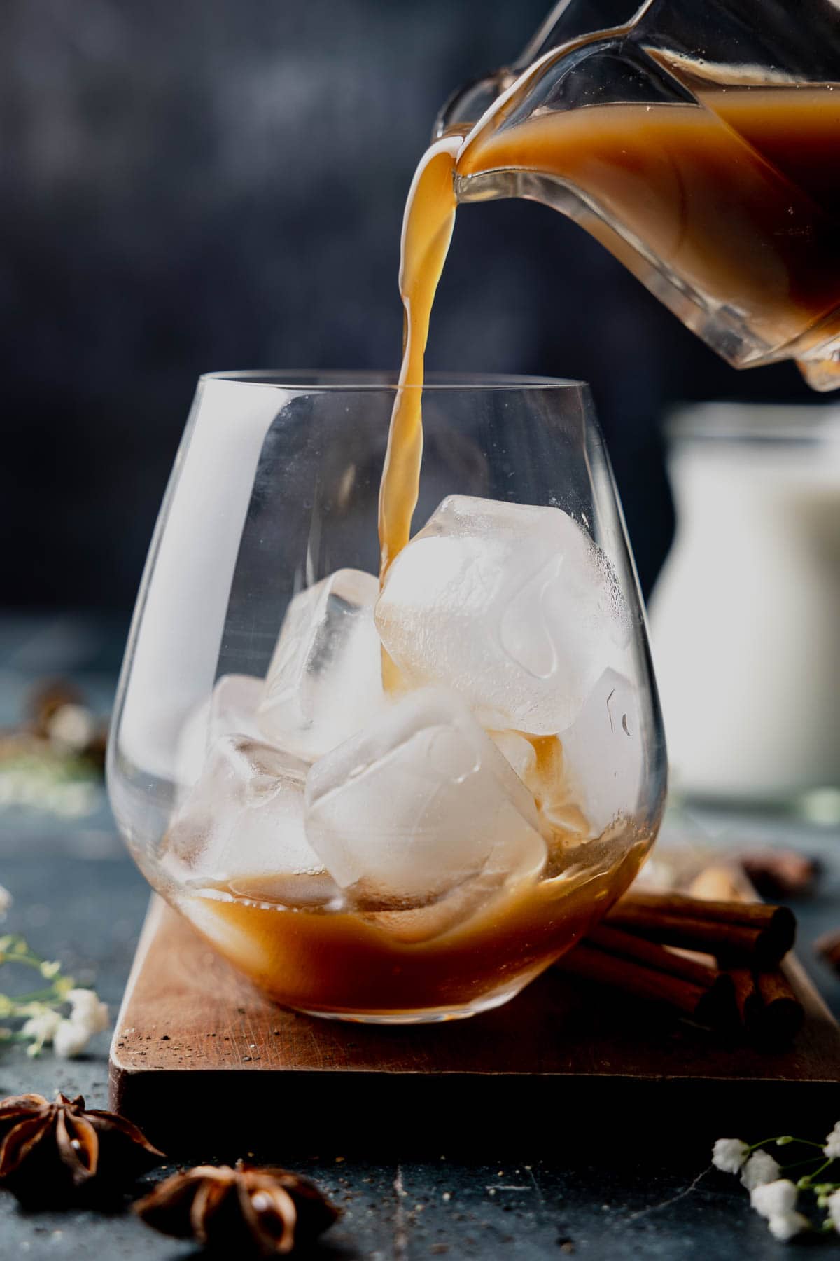 Pouring chai tea concentrate into stemless wine glass filled with ice. 