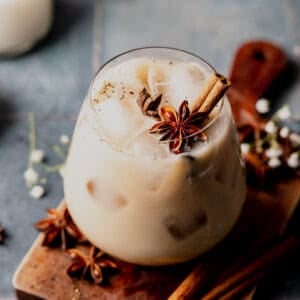 Starbucks copycat iced chai latte in a stemless wine glass garnished with star anise and cinnamon stick, on blue tile surface.