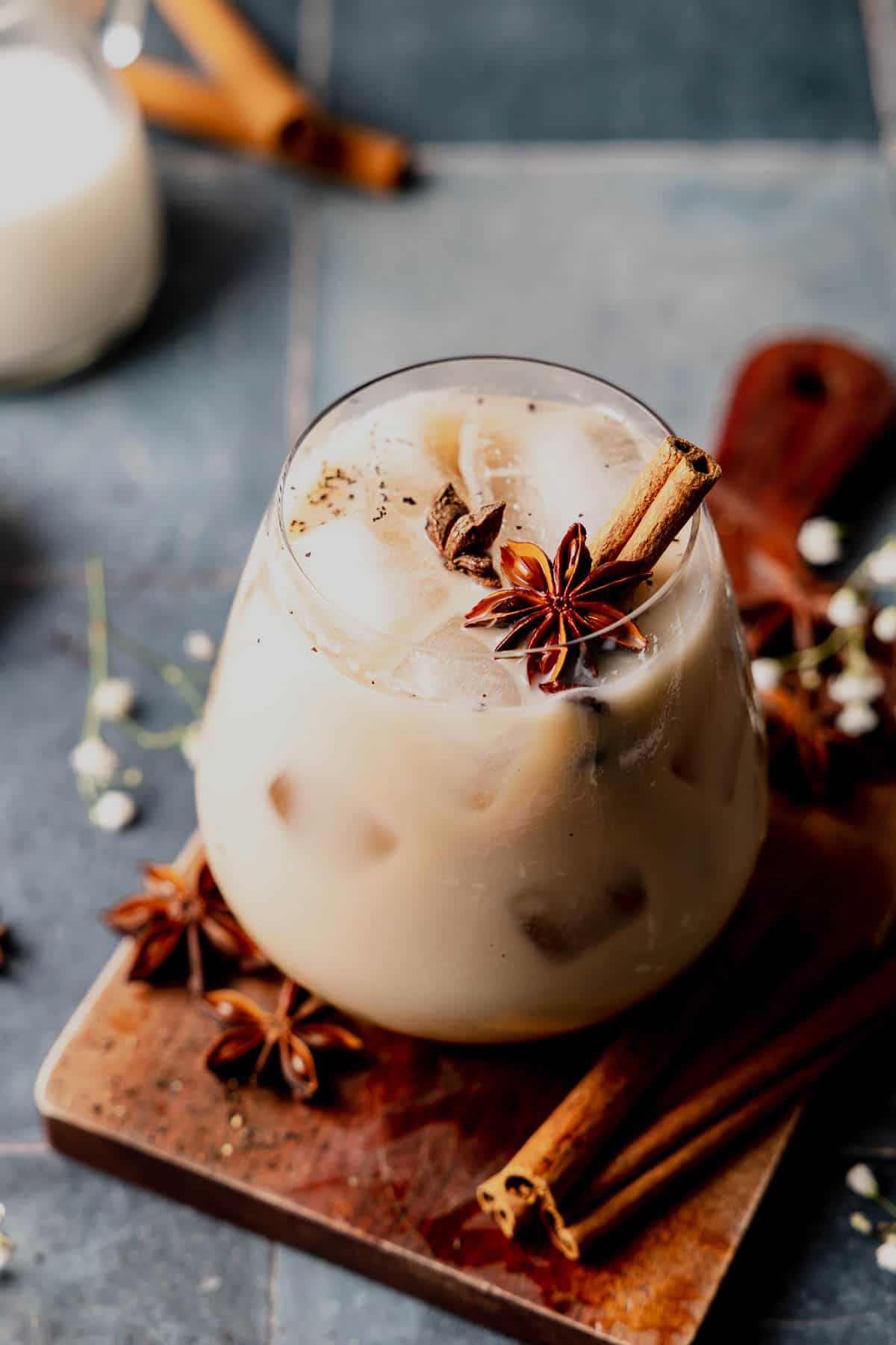 Starbucks copycat iced chai latte in a stemless wine glass garnished with star anise and cinnamon stick, on blue tile surface.