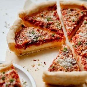 Gluten free Chicago deep dish pizza with sauce on top, sliced and resting on parchment paper, sprinkled with parmesan and parsley.