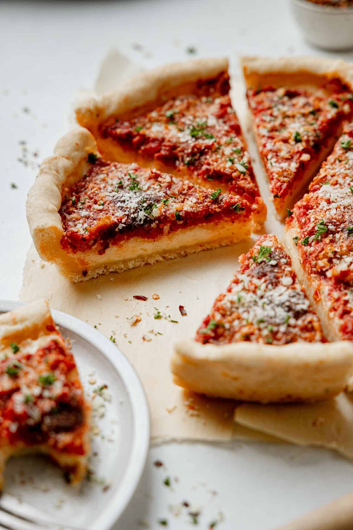 Gluten free Chicago deep dish pizza with sauce on top, sliced and resting on parchment paper, sprinkled with parmesan and parsley.