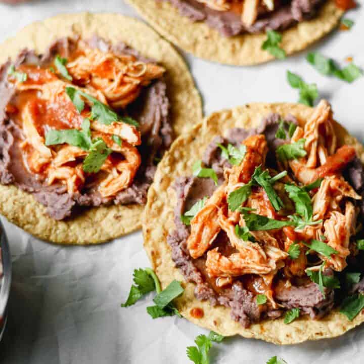 Shredded chicken Tinga on top of tostadas with refried black beans and cilantro.