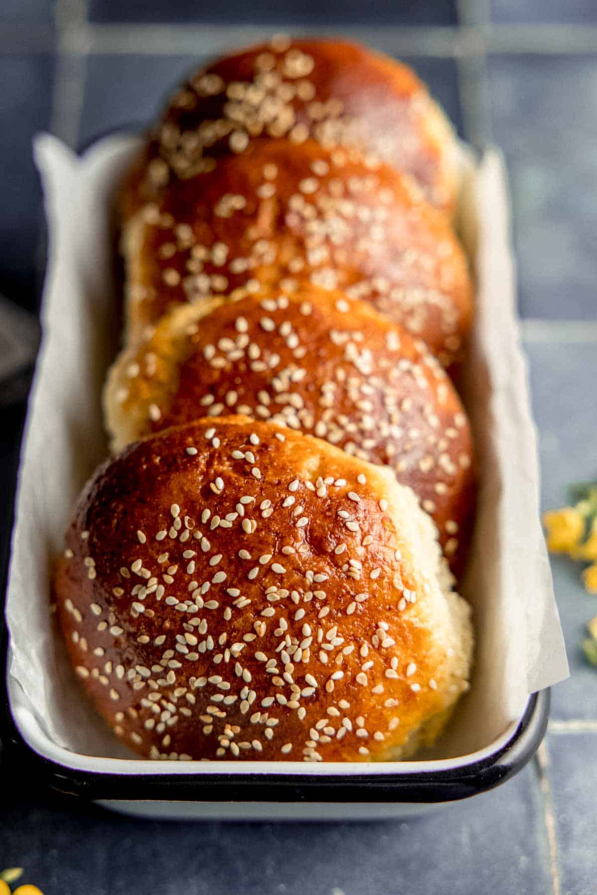 Gluten free hamburger buns with sesame seeds lined up in a loaf pan.