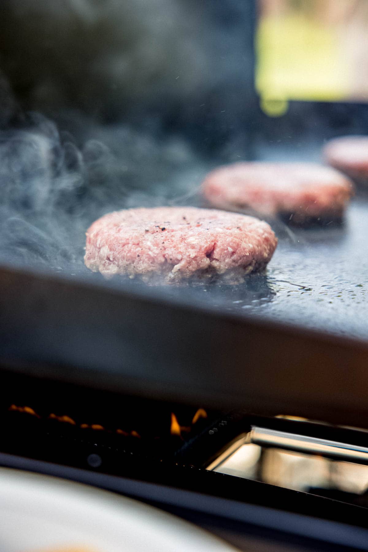 Sizzling hamburger patties cooking on a Blackstone griddle.