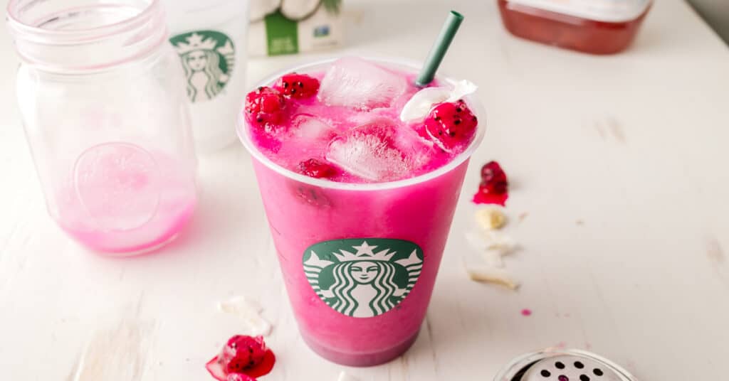 Bright purple Starbucks dragon drink in Starbucks cup garnished with dragon fruit and coconut.