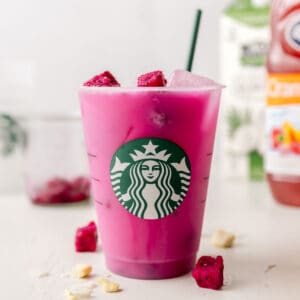 Starbucks dragon drink in a Starbucks cup with green straw and dragon fruit pieces.