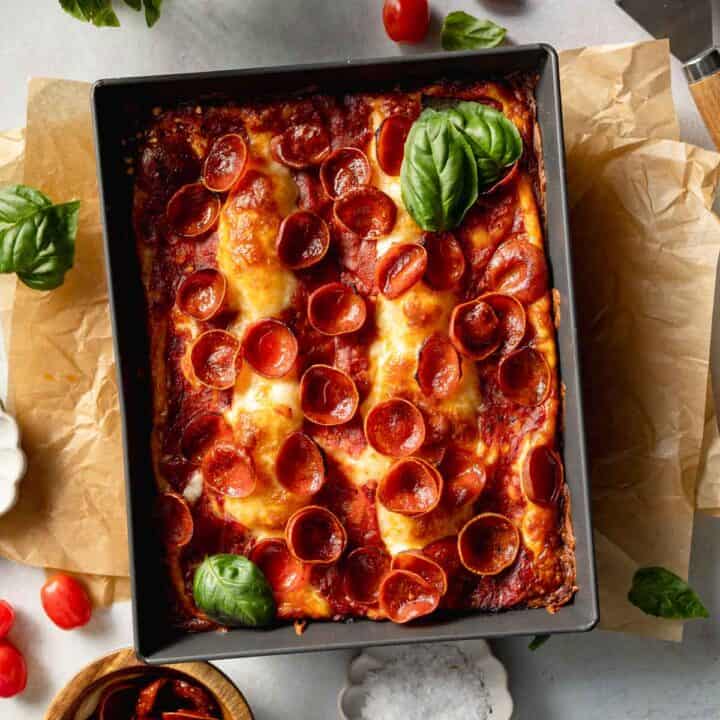 A gluten-free Detroit pizza topped with pepperoni and basil in dark pan.