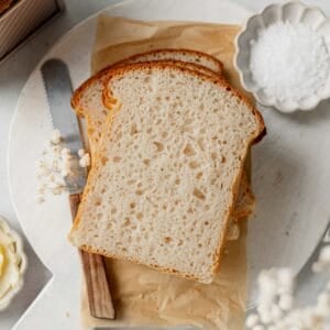 Slices of gluten-free sourdough sandwich bread stacked on a piece of parchment paper.
