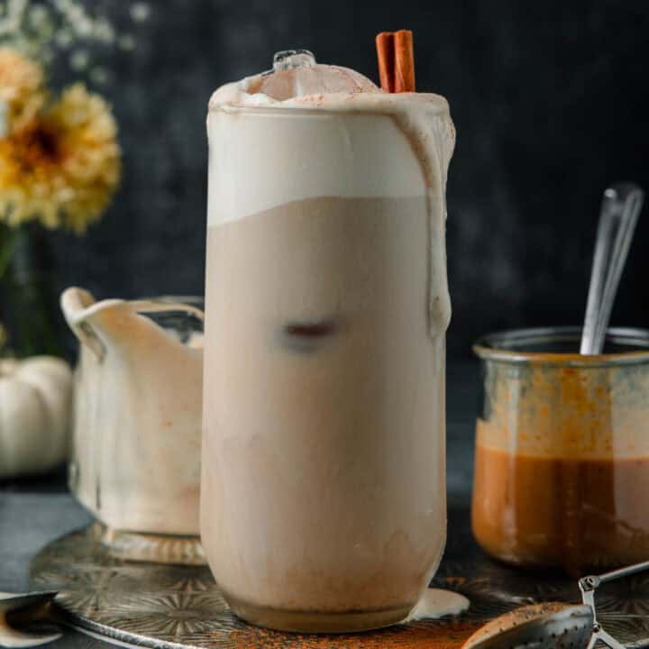 A homemade iced pumpkin chai latte in a tall glass with pumpkin cold foam spilling over the top.